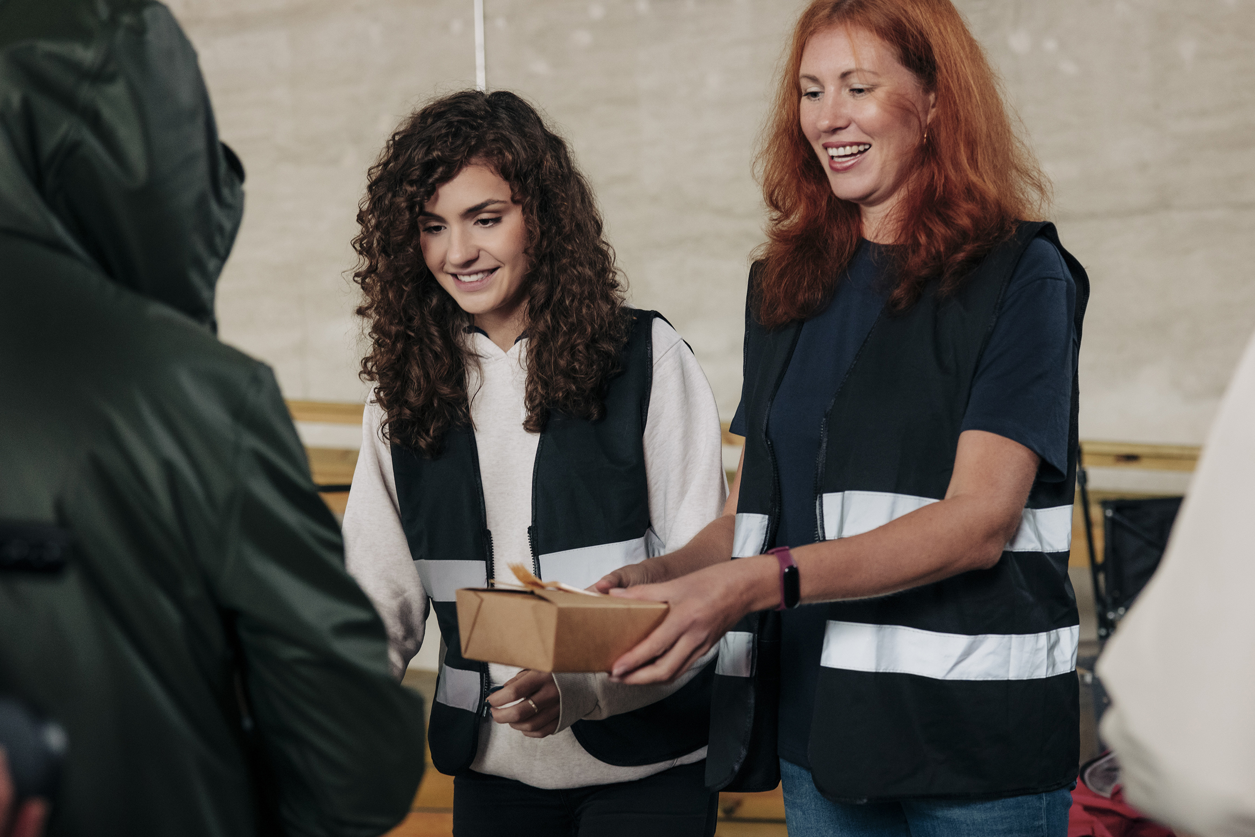 Smiling female volunteers distributing food boxes to homeless people at community center